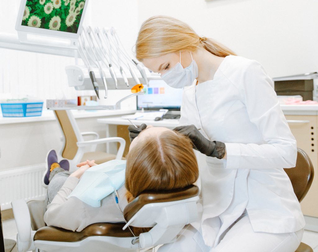 Photo of woman in white scrub suit examines the dental health of a patient